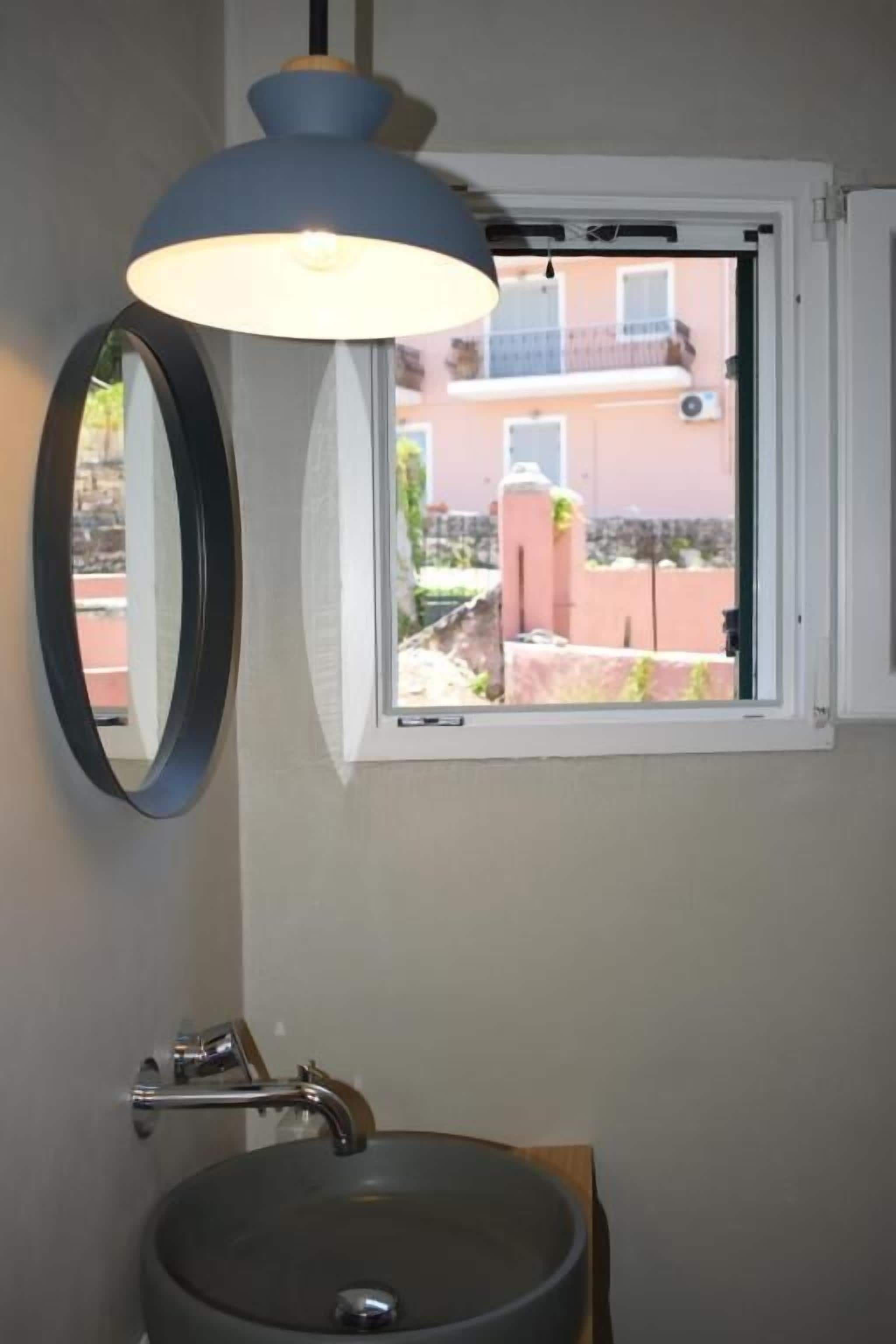 A bathroom with a round mirror, a sink, a window, and a pendant light.