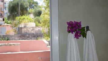 Et vindue med udsigt til en bygning og grønne planter, et hvidt håndklæde og en lilla blomst.