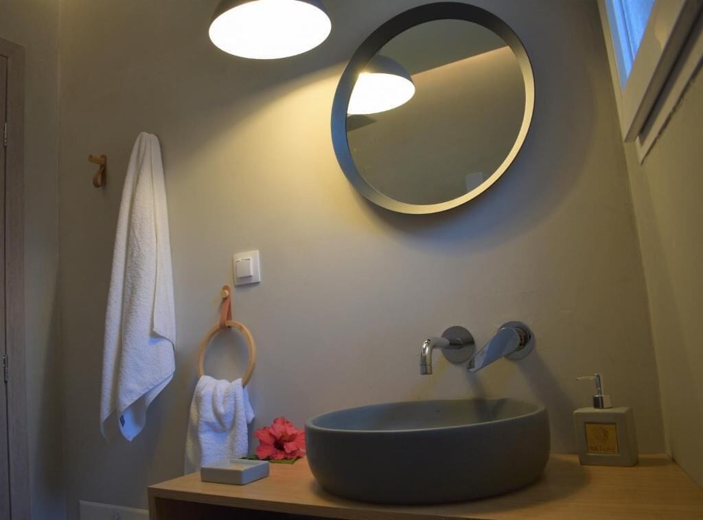 A bathroom with a round mirror, a round sink, a towel rack, and a small bottle of soap.