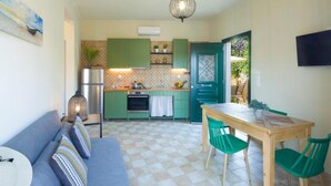 Una cocina compacta con armarios verdes, una mesa de comedor de madera y un sofá con cojines a rayas.