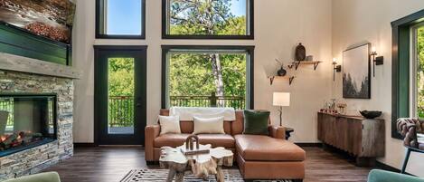 A spacious living room with a stone fireplace, a large window, a leather sofa, and a wooden coffee table.