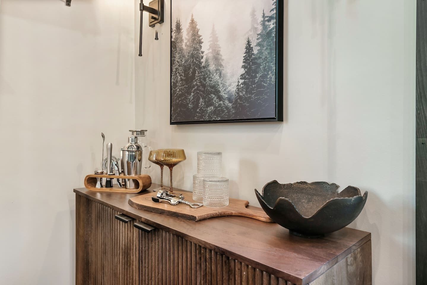 Un meuble en bois orné d’un saladier décoratif, d’un tableau encadré et d’un luminaire fixé au mur.