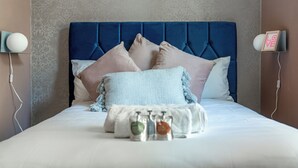 Ein ordentlich bezogenes Bett mit blauem Kopfteil, mehreren Kissen und einem dekorativen Gegenstand.