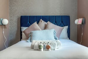 Una cama bien hecha con cabecera azul, varios almohadones y un adorno sobre la cama.