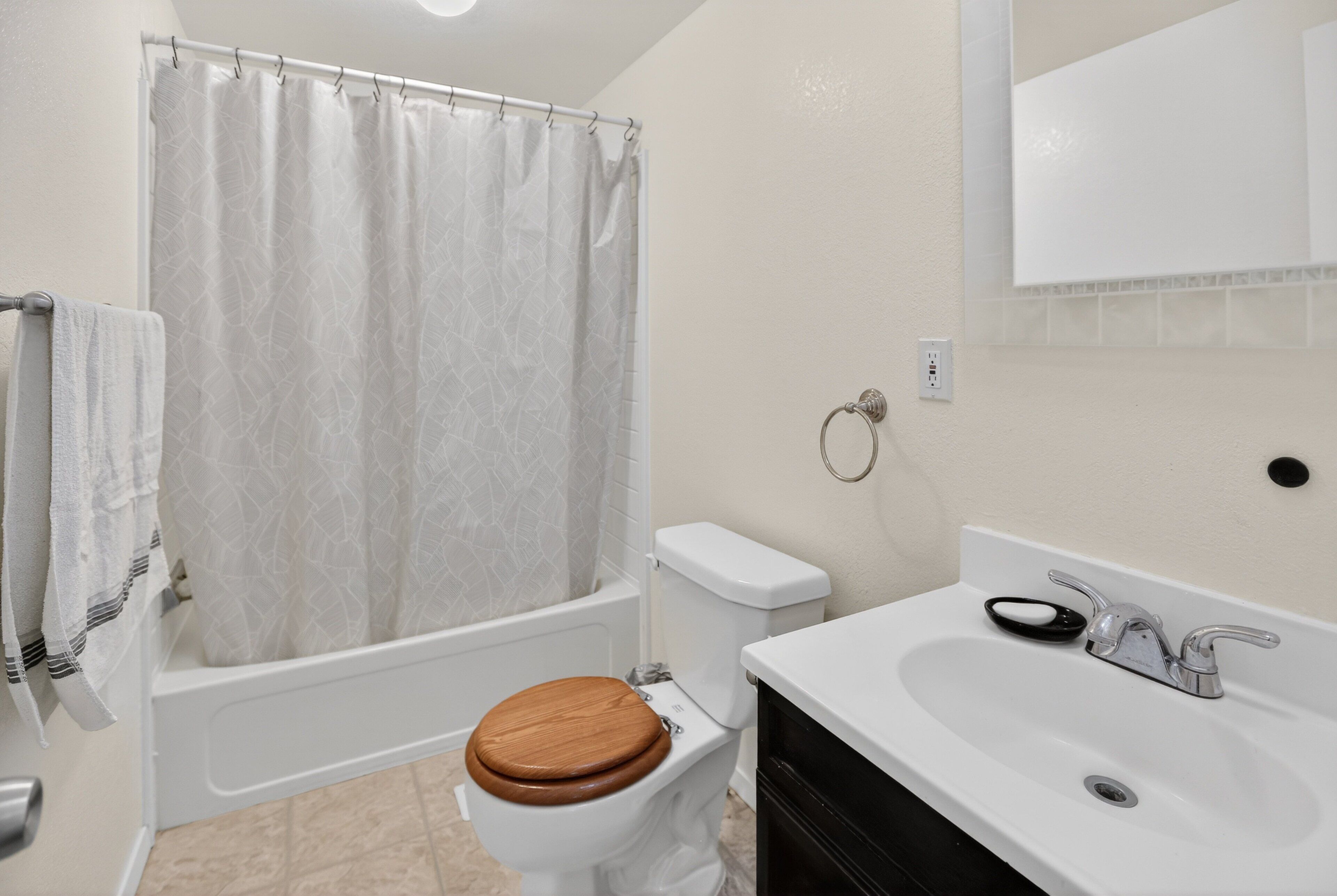 A bathroom with a toilet, bathtub, shower curtain, sink, and mirror.
