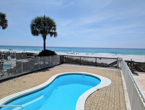 Ein Pool mit geschwungener Kante, eine Holzterrasse und Blick auf Strand und Meer.