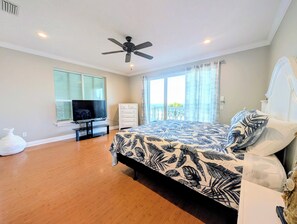 Ein Schlafzimmer mit einem Bett, einem Deckenventilator, einem Fernseher, einer Kommode und einem Fenster mit Jalousien.