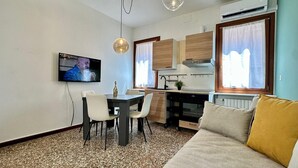 Un espacio habitable compacto con una mesa de comedor, sillas, un sofá, una zona de cocina y un televisor montado en la pared.
