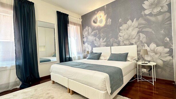 Un dormitorio con una cama grande, una mesita de noche, un espejo y un papel tapiz con motivos florales.