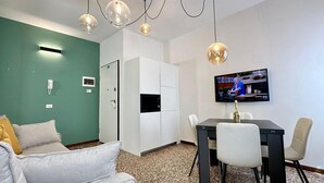 Una habitación con pared verde, un armario blanco, un televisor en la pared, una mesa de comedor con sillas y un sofá.