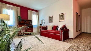 Ein Wohnzimmer mit einem roten Sofa, einem beigen Teppich, einem Holzschrank und einer Pflanze.