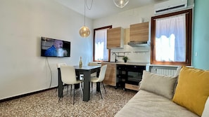 A compact living space with a dining table, chairs, a sofa, a kitchen area, and a television mounted on the wall. - Residence Marina (Historical Center) (Venice)