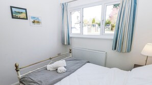 A hotel room with a bed, a window with curtains, a radiator, and two framed pictures on the wall. - Moonraker (Saundersfoot)
