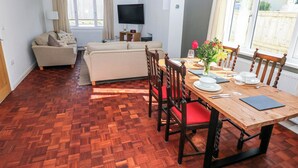 A dining area with a wooden table, chairs, and a television in the background. - Moonraker (Saundersfoot)