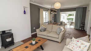 A living room with a sofa, a wooden coffee table, a fireplace, and a dining area with a table and chairs. - Moonraker (Saundersfoot)