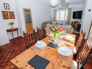 Ein Essbereich mit einem Holztisch, gedeckt für vier Personen, Stühlen, einer Blumenvase und einem Fernseher im Hintergrund.