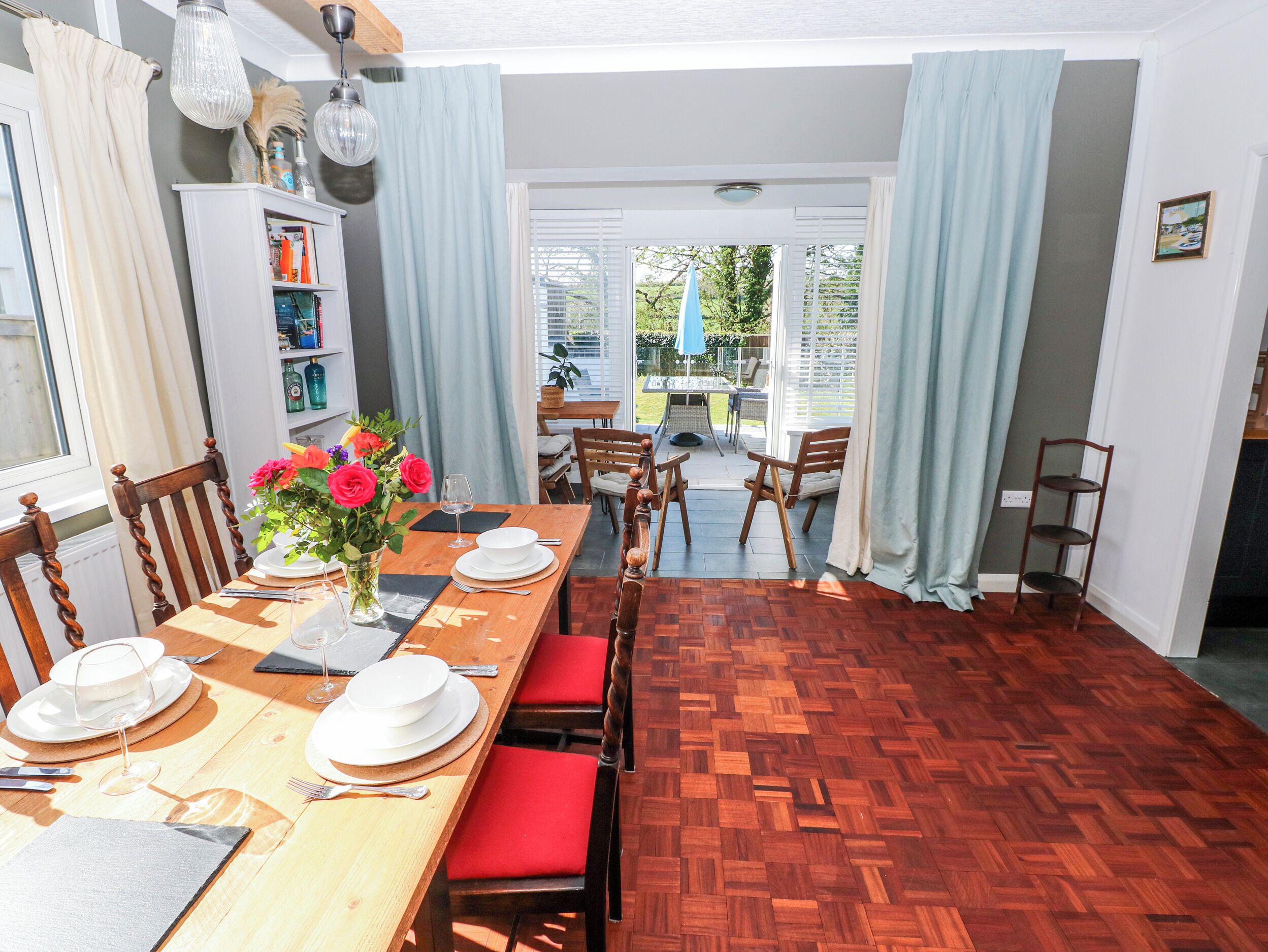 Een eetgedeelte met een houten tafel gedekt voor vier personen, rode fauteuils, een bloevas en een boekenkast.