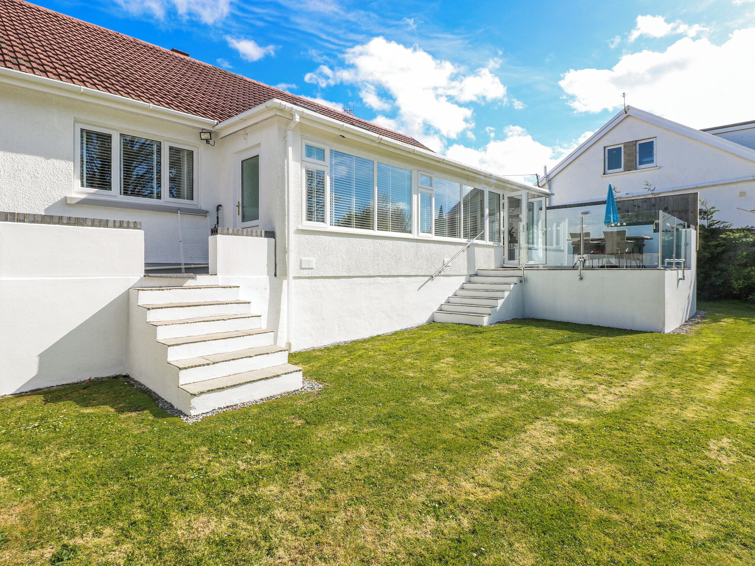 A modern house with a white exterior, a red-tiled roof, and a small outdoor seating area.
