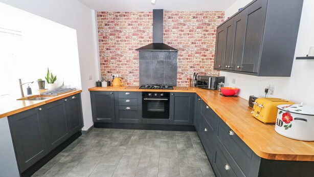 A modern kitchen with dark cabinetry, a brick backsplash, a gas stove, and a toaster. - Moonraker (Saundersfoot)
