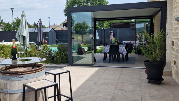 An outdoor patio with a glass enclosure, a wooden barrel, and a table with chairs. - Le Clos Carion A little corner of paradise just a stone's throw from the town center (Autun)
