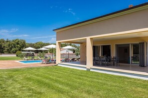 Uma casa moderna com varanda coberta, piscina e gramado bem cuidado.
