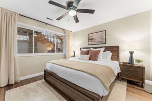 Ein Schlafzimmer mit einem Bett, einem Nachttisch, einer Lampe, einem Deckenventilator und einem Fenster.