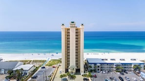 A tall hotel with a central courtyard, beachfront view, and a parking lot. - Luxurious & Private, Beach Front, Pool, 3BD/2BA, 1800 SqFt, Large Balcony (Panama City Beach)