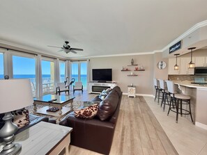 A spacious living area with a sofa, dining table, and bar stools, a flat-screen TV, and a view of the ocean. - Luxurious & Private, Beach Front, Pool, 3BD/2BA, 1800 SqFt, Large Balcony (Panama City Beach)