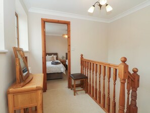 A hallway with a wooden staircase, a mirror, and a bed in the adjacent room. - 1 The Stables (Wrexham)