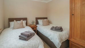 Un dormitorio con dos camas, una mesita de noche con lámpara y un armario de madera.