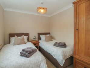 A bedroom with two beds, a nightstand with a lamp, and a wooden wardrobe. - 1 The Stables (Wrexham)