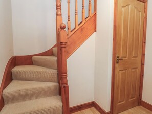 A wooden staircase with a handrail, carpeted steps, and a wooden door. - 1 The Stables (Wrexham)