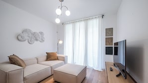 Ett modernt vardagsrum med en soffa, en pall, en platt-TV och en taklampa.