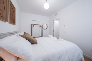 Ein ordentlich bezogenes Bett mit weißen Leinen, einem Holz-Kopfbrett und einem einzelnen braunen Kopfkissen.