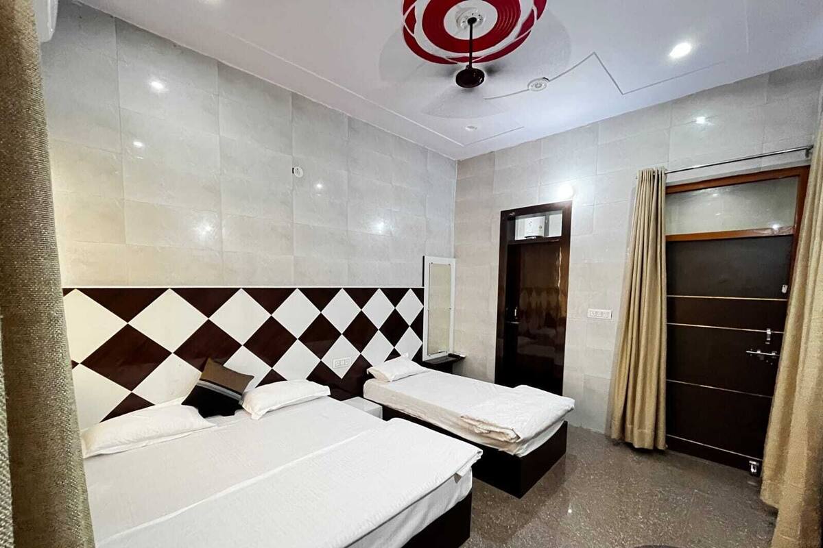 A hotel room with two beds, a mirror, a door, and a ceiling fan.