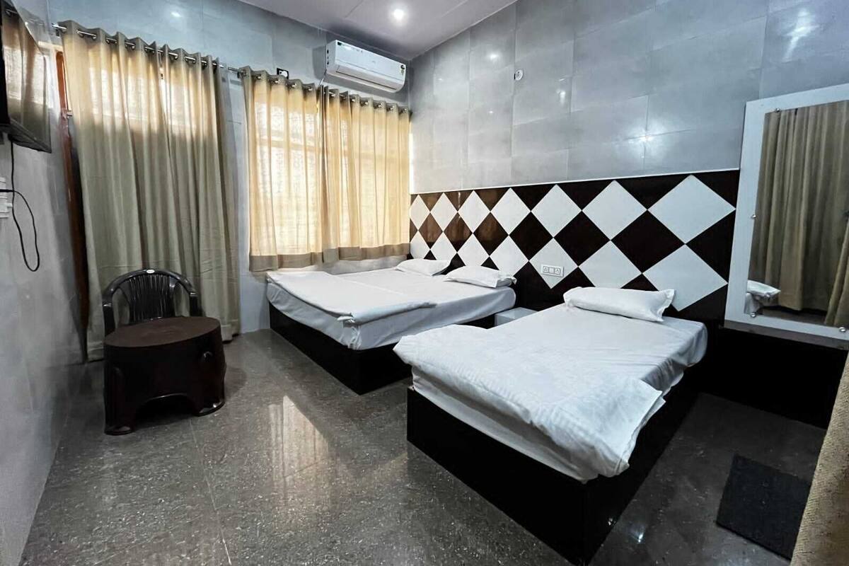 A hotel room with two beds, a chair, a small table, and an air conditioning unit.