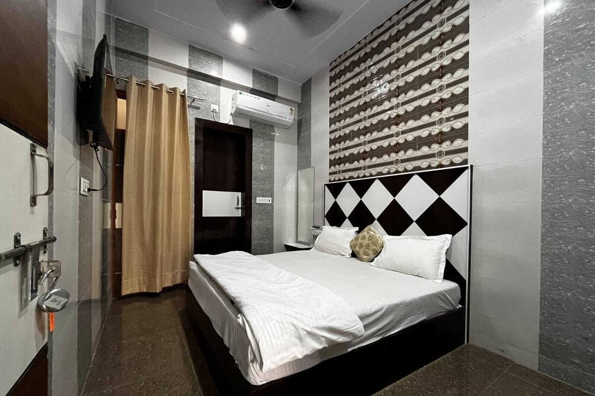 A hotel room with a bed, a shower area, a towel rack, and a wall-mounted air conditioning unit.