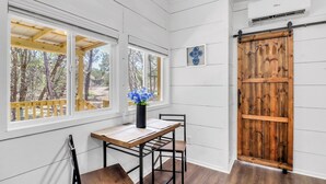 A room with a wooden table, two chairs, a potted plant, and a large wooden door. - Charming Tiny Home Retreat | Porch Swing, Grill, Stargazing Near Caverns (Bulverde)