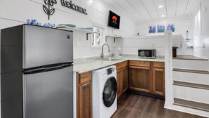 A modern kitchen with a stainless steel refrigerator, a washing machine, wooden cabinets, a sink, and a microwave. - Charming Tiny Home Retreat | Porch Swing, Grill, Stargazing Near Caverns (Bulverde)