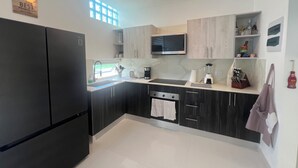 Una cocina moderna con un refrigerador negro, un microondas, un lavamanos y un ventanal con persianas.