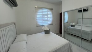 Un dormitorio con cama, ventana con persianas, espejo y aire acondicionado.