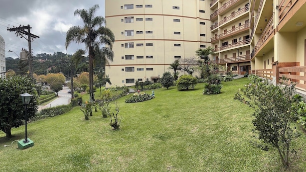 A multi-story building with balconies, a well-maintained lawn, and a street in the background. - Apartment in the Tourist Center with 24-hour Reception/Concierge (Campos do Jord ão)