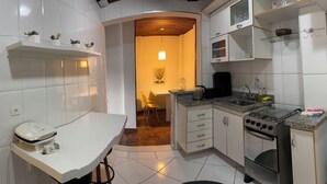 A compact kitchen with white cabinets, a stove, a microwave, and a refrigerator. - Apartment in the Tourist Center with 24-hour Reception/Concierge (Campos do Jordão)
