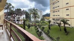 A balcony with a view of a courtyard, a building with multiple windows, and a tree. - Apartment in the Tourist Center with 24-hour Reception/Concierge (Campos do Jordão)