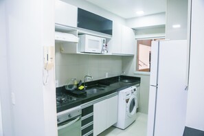 Uma cozinha compacta com micro-ondas, fogão, pia e máquina de lavar.