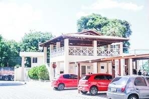 Um edifício com entrada coberta, uma pequena varanda e um carro vermelho estacionado em frente.