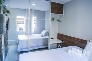 Quarto de hotel com cama, escrivaninha, televisão e janela com cortinas.