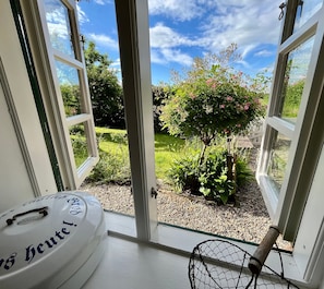 Udsigt gennem åbne franske døre ud til en have med et hvidt bord og en træstol.