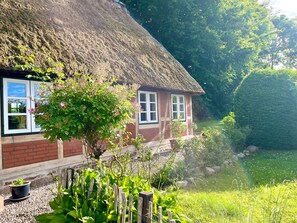 Et hus med stråtækt tag og murstensfacade, med vinduer og en have med et bassin.