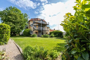A two-story building with a balcony, surrounded by a well-maintained lawn and various shrubs.